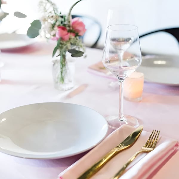 A beautifully set table at Cafe POM with a white plate, gold cutlery, pink napkin, wine glass, and floral centerpiece.