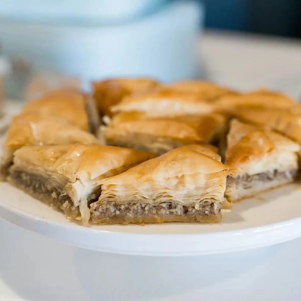 A close-up of golden-brown baklava pieces with flaky pastry and a nut filling on a white plate.