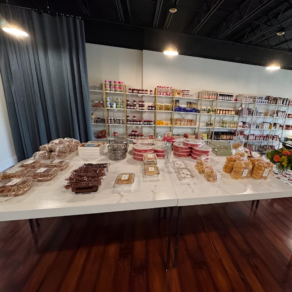A long white table filled with packaged Mediterranean pastries and baked goods, with shelves of products in the background.