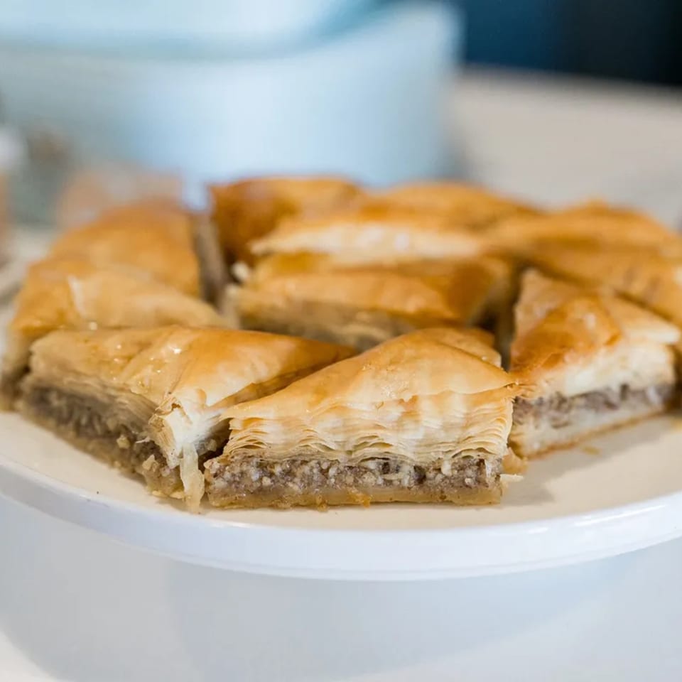 Triangular pieces of golden-brown baklava with a nutty filling arranged on a white plate.
