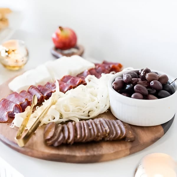 A Mediterranean charcuterie board with sliced meats, cheeses, olives, and a pomegranate.