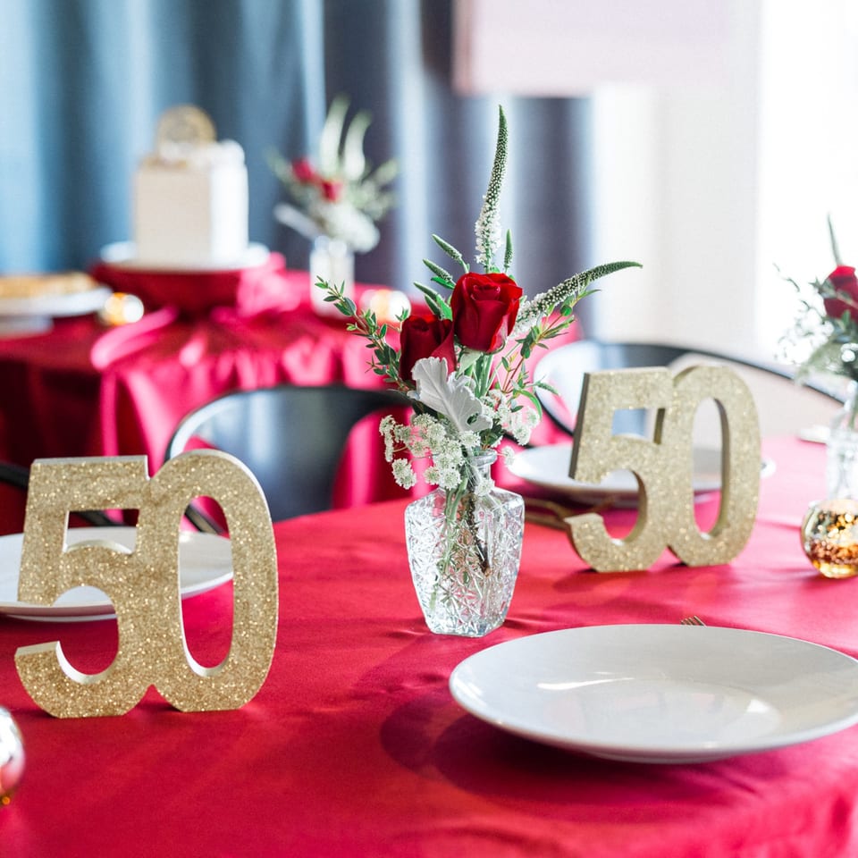 A festive table set with a red tablecloth, glittery '50' decorations, and red rose centerpieces.