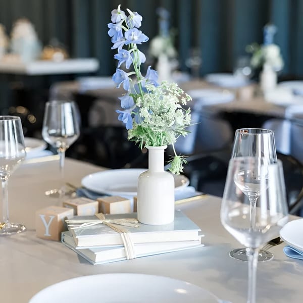 Elegant table setting at Cafe POM with a white vase of blue flowers, books, and wine glasses.
