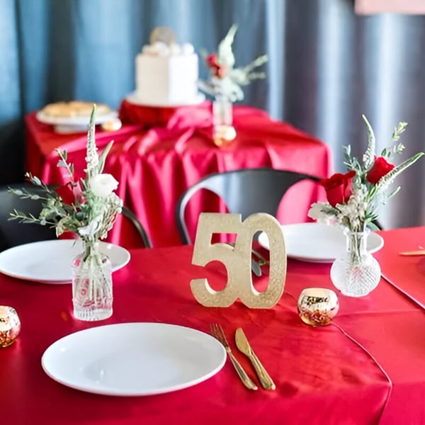 A festive table set with red tablecloths, white plates, gold cutlery, and floral centerpieces.