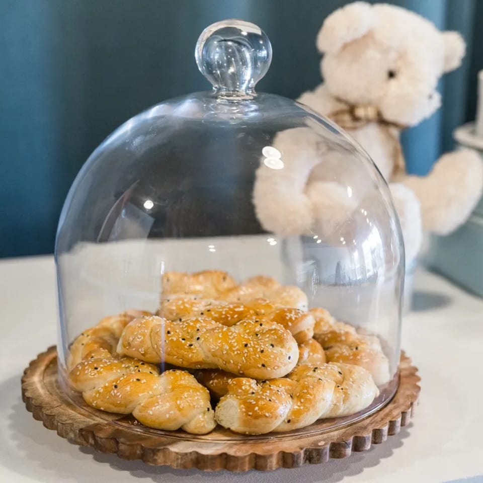 Mediterranean pastries with sesame seeds under a glass cloche, with a teddy bear in the background.