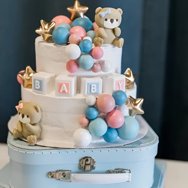Two-tier baby shower cake with teddy bears, stars, and "BABY" blocks, on a blue suitcase.