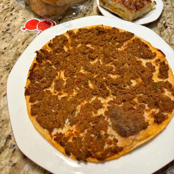 A round Mediterranean flatbread topped with spiced ground meat, served on a white plate.