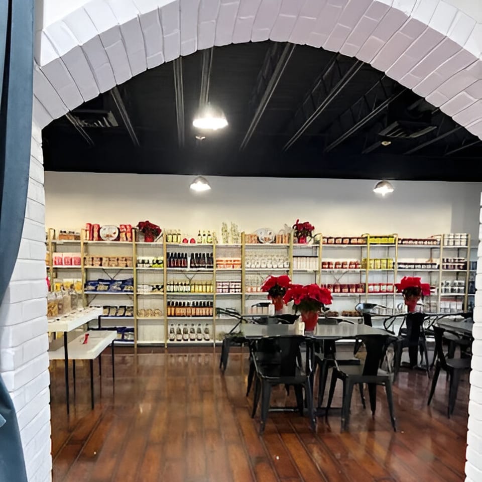 Cafe POM's dining area with black tables and chairs, shelves of Mediterranean products, and poinsettias.