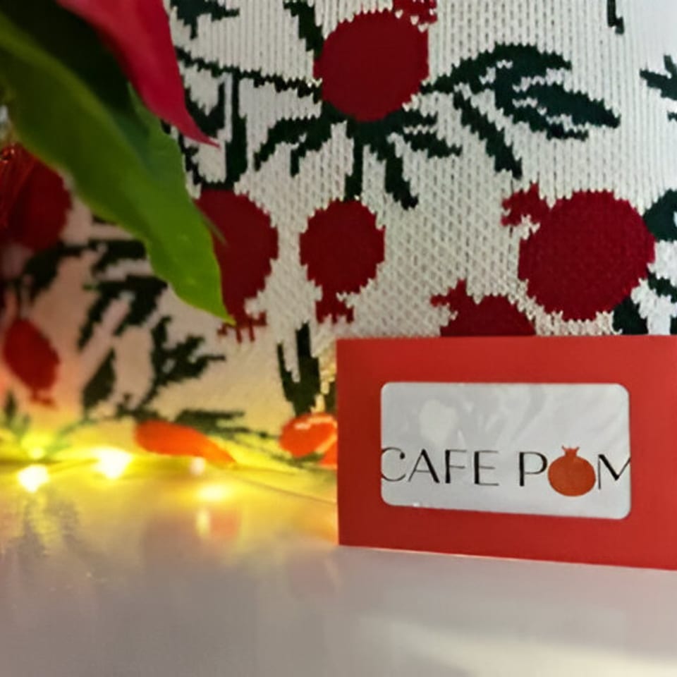 Cafe POM business card with a pomegranate design, fairy lights, and a pomegranate-patterned fabric.