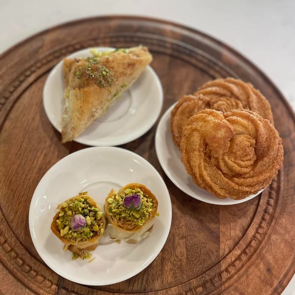 Mediterranean desserts: baklava, pistachio bird's nests, and fried pastries on a wooden tray.