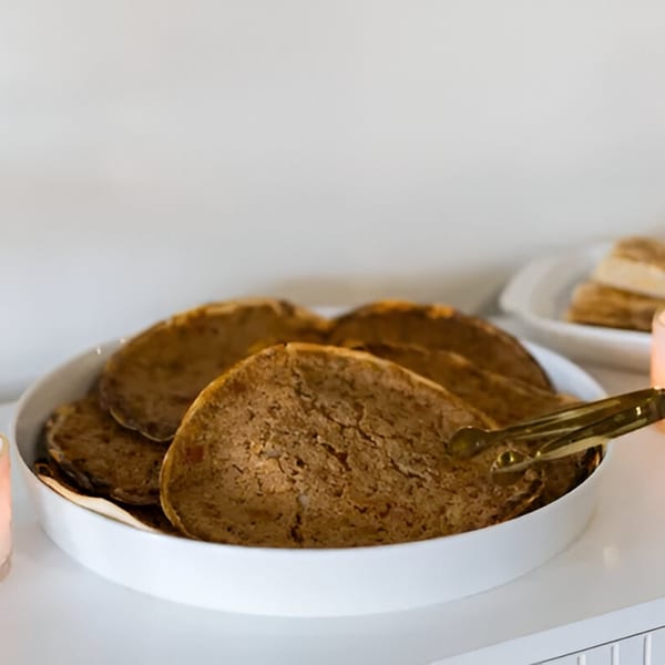 A white bowl filled with several round, brown flatbreads, with tongs resting on the side.