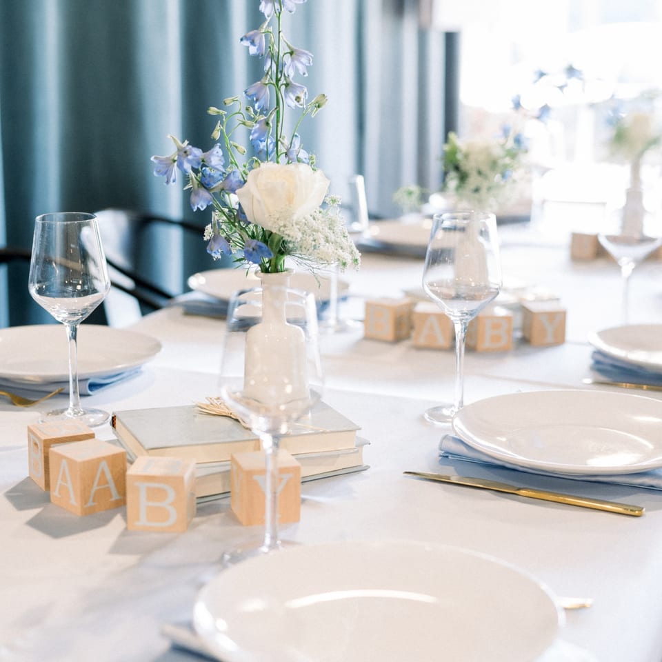 Elegant table setting with white plates, wine glasses, blue flowers, and "BABY" blocks at Cafe POM.