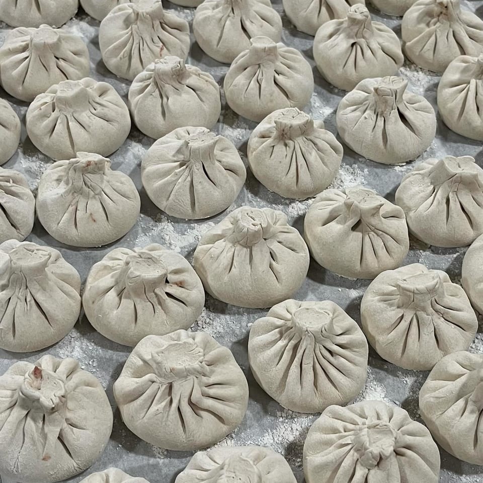 Rows of uncooked khinkali, Georgian dumplings, dusted with flour on a gray surface.