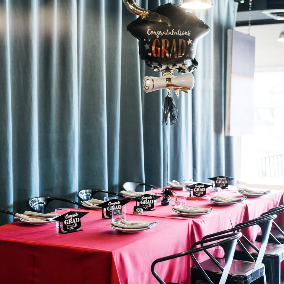 A graduation party table with a pink tablecloth, place settings, and "Congrats Grad" decorations.